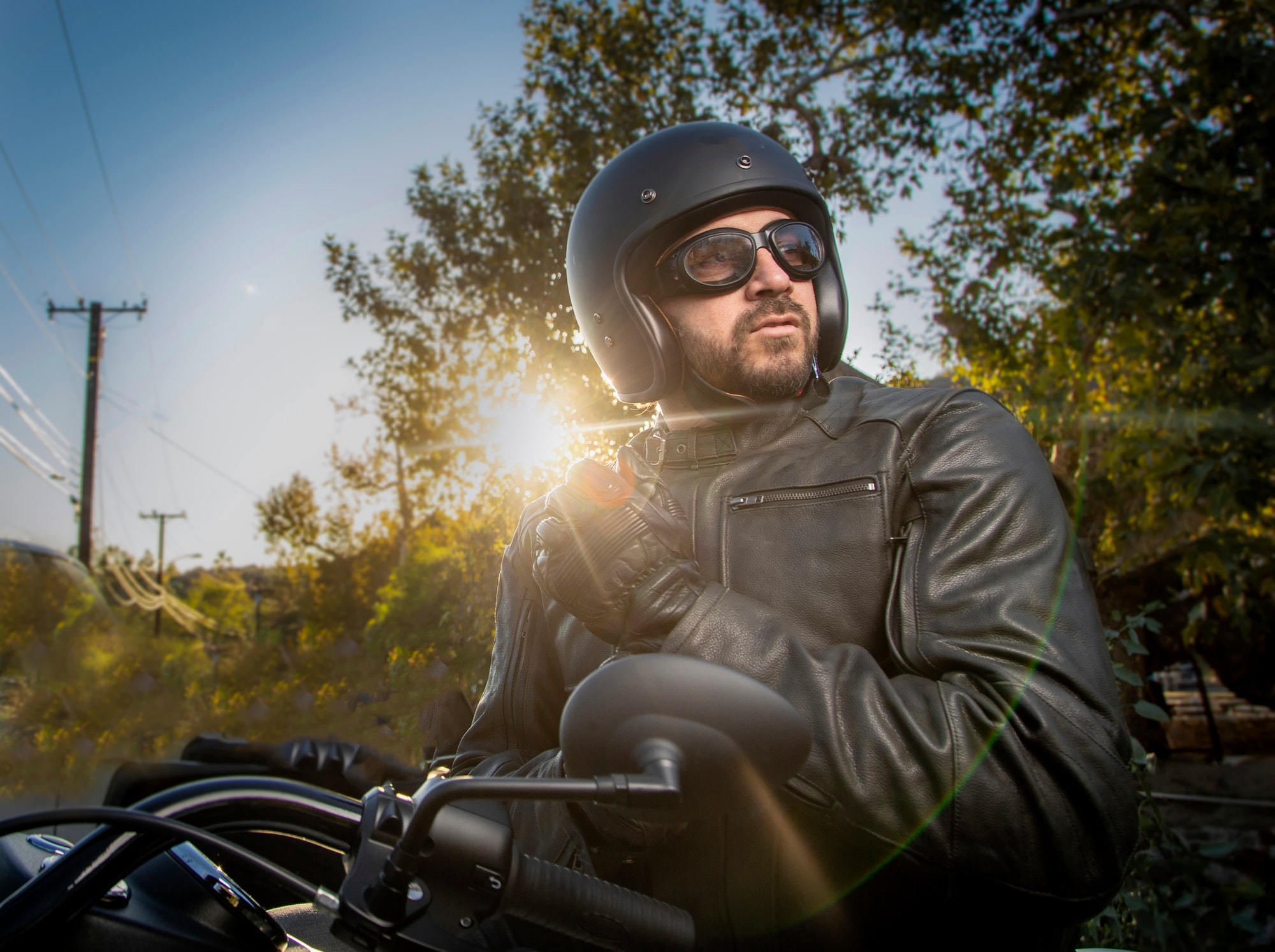Motorcycle rider looking camera right wearing leather jacket, gloves, goggles and helmet